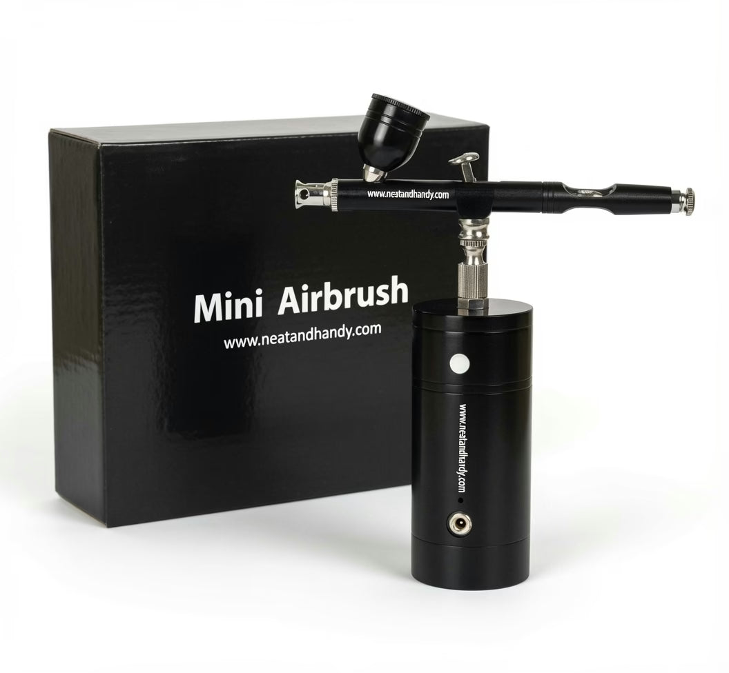 A black mini airbrush tool with a cylindrical body and angled spray arm, shown in front of a black branded box labeled 'Mini Airbrush' and 'www.neatandhandy.